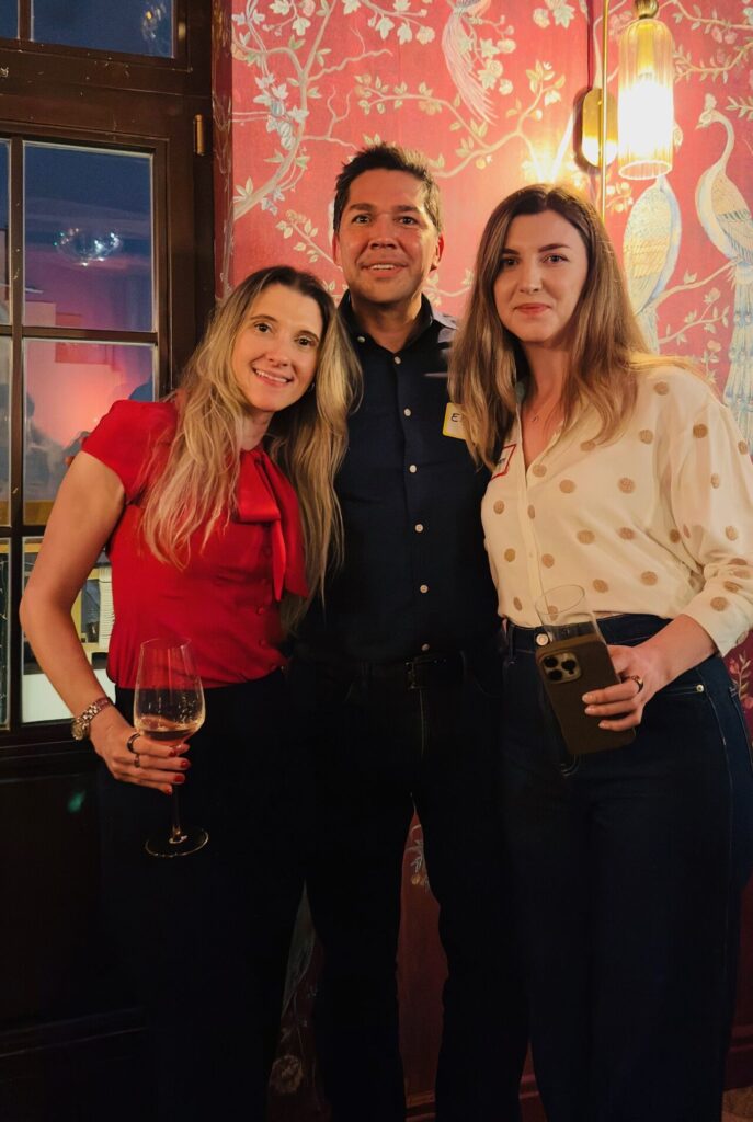 Eric Melchor wearing a name tag posing with two women at a cocktail party, one holding a glass of wine