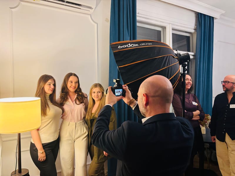 Photographer capturing three smiling women posing together, with a large softbox light and blue curtains in the background